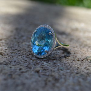 Custom designed lady's oval blue topaz ring with diamond halo and split shank in white gold