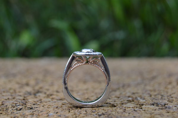 Custom designed engagement ring with bezel set round diamond with halo and milgrain beading in white and rose gold and treated green diamond accent peek a boo