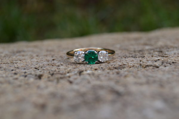 Custom designed two tone three stone ring with one round emerald and two round diamonds all prong set