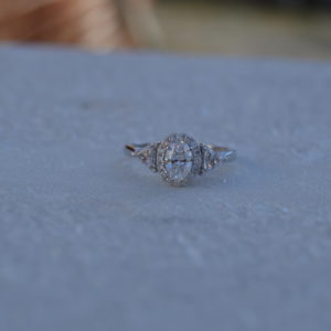 Oval diamond halo engagement ring with trillion shaped diamonds on the side in white gold