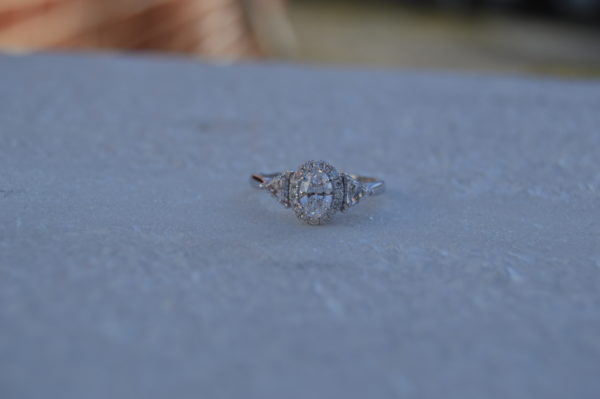 Oval diamond halo engagement ring with trillion shaped diamonds on the side in white gold